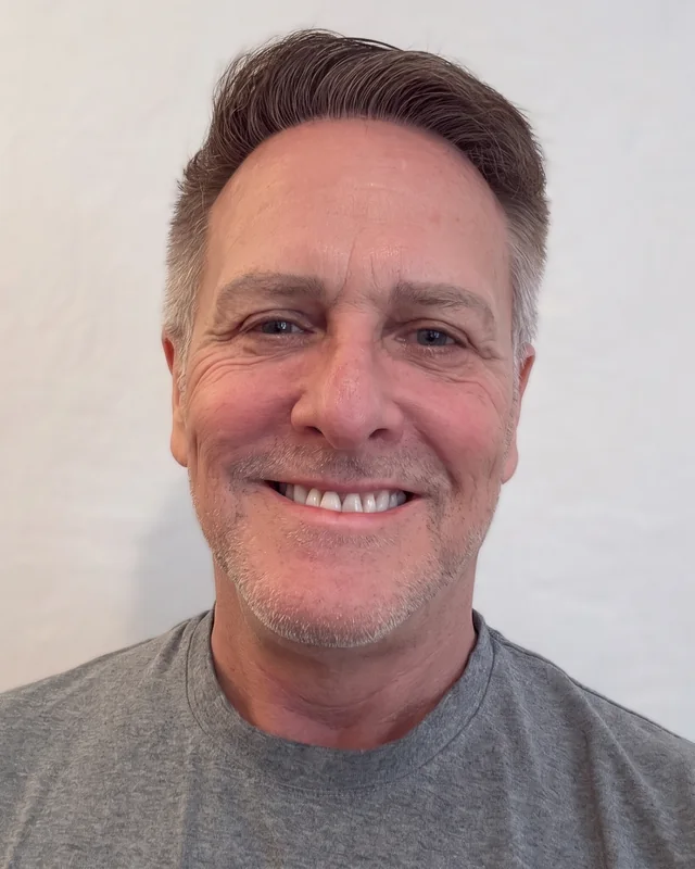 Eric Pendleton, smiling, in a grey T-shirt against a white wall.