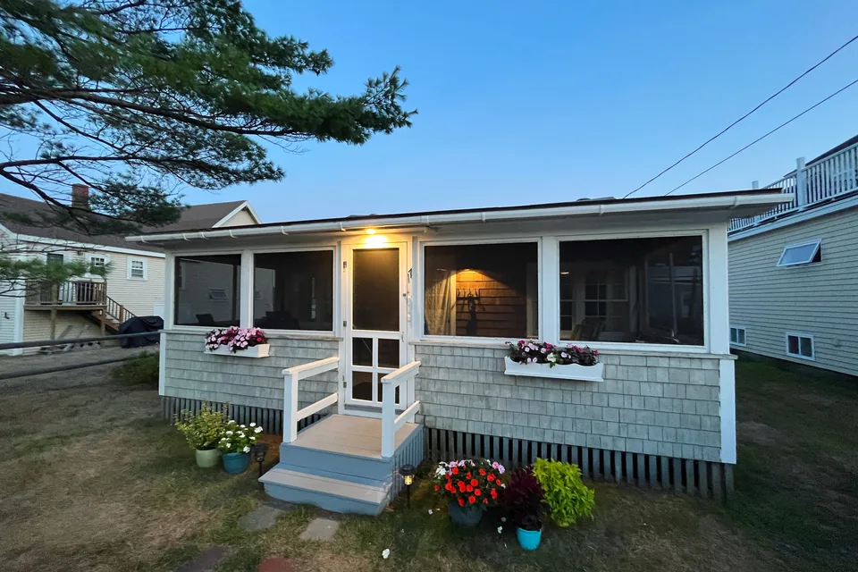 The cottage at evening with its lights on and flowers out front.