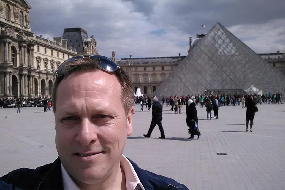 Eric in a selfie in the Louvre's courtyard, the glass pyramid behind him.